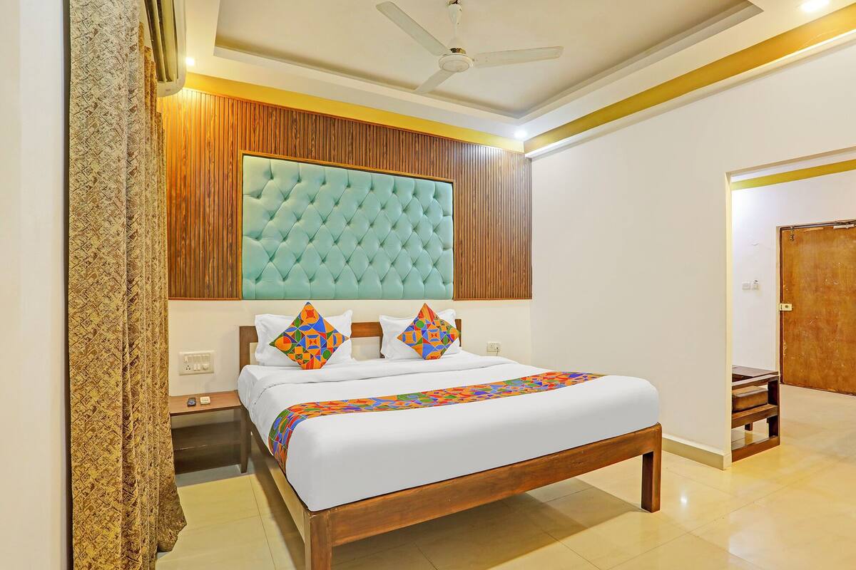 A bedroom with a wooden headboard, a bed with colorful pillows, a ceiling fan, and a wooden bench in the corner.