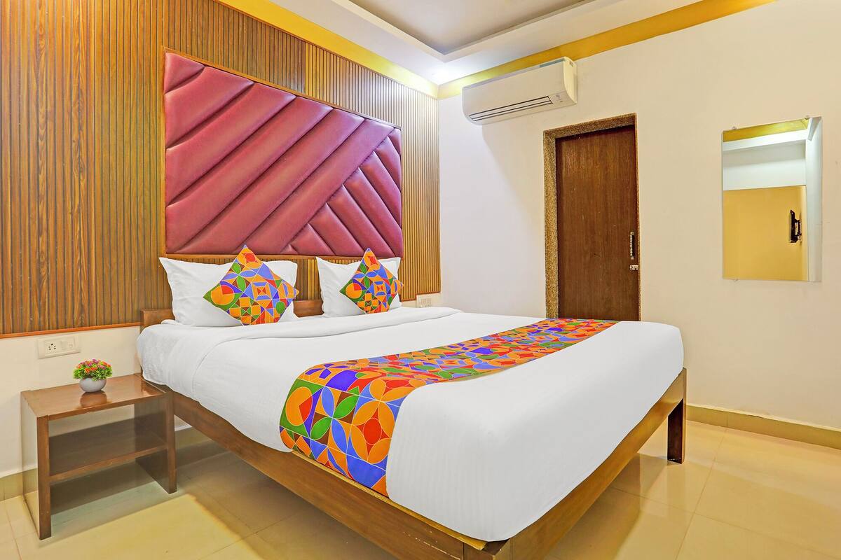 A hotel room with a large bed, a wooden headboard, a nightstand with a plant, and a mirror on the wall.