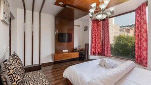 Un dormitorio con techo de madera, televisor montado en la pared, cama con ropa blanca y ventana con cortinas rojas.