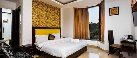 A hotel room with a large bed, a ceiling fan, a window with curtains, and a desk with a chair.