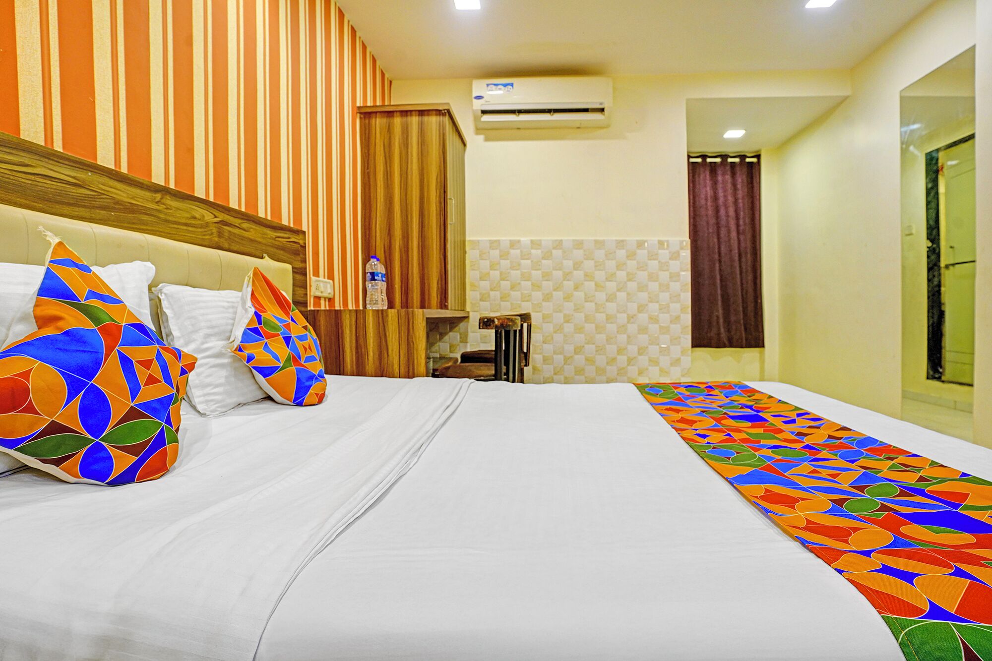 Une chambre d’hôtel avec un lit, un papier peint à rayures, un appareil de climatisation et une salle de bain visible à travers une porte ouverte.