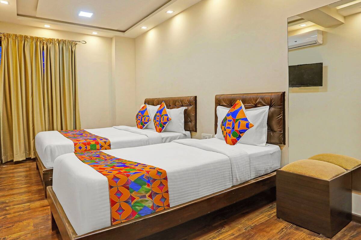 A hotel room with two beds, a wooden floor, a curtain, and an air conditioning unit.