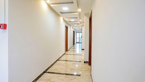 A long, well-lit hallway with a fire alarm on the left, leading to a door at the end. - FabHotel Pooja - Near Bagalur Main Road (Bangalore)