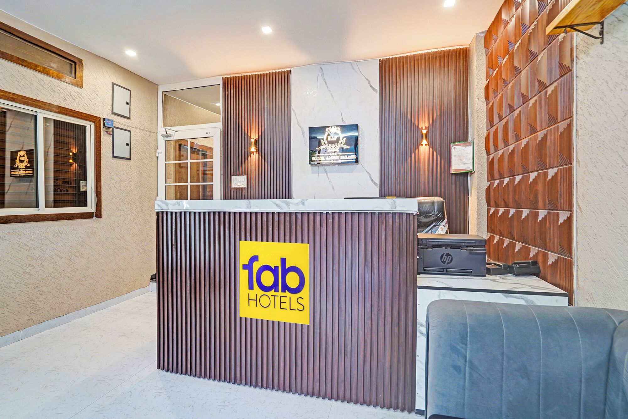A hotel reception desk with a 'fab hotels' sign, a reception area with a wooden panel wall, and a seating area with a blue chair.