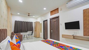 A hotel room with a bed, a desk, a chair, a wardrobe, a television, and an air conditioning unit. - Fabhotel Amrit Palace - Opp Skye Corporate park (Indore)