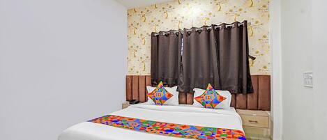 Une chambre à coucher avec un lit, des rideaux, une table de chevet et un mur orné d’un motif floral.