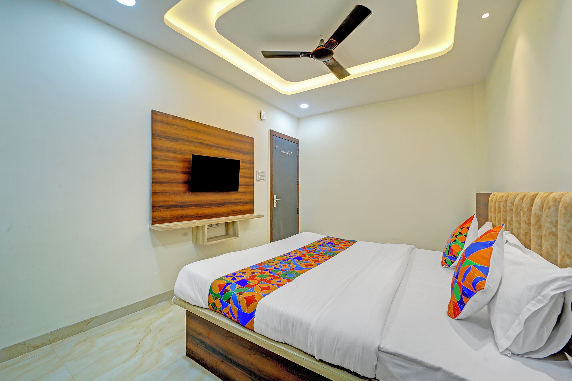 Un dormitorio moderno con cama, ventilador de techo, televisor montado y una puerta.