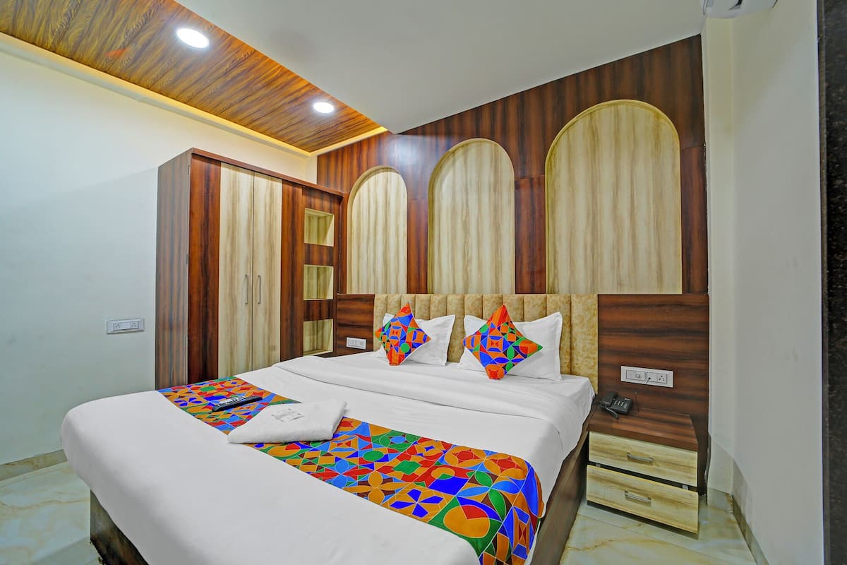 A bedroom with a wooden headboard, a bed with a colorful geometric-patterned bedspread, and a bedside table with a phone and remote control.