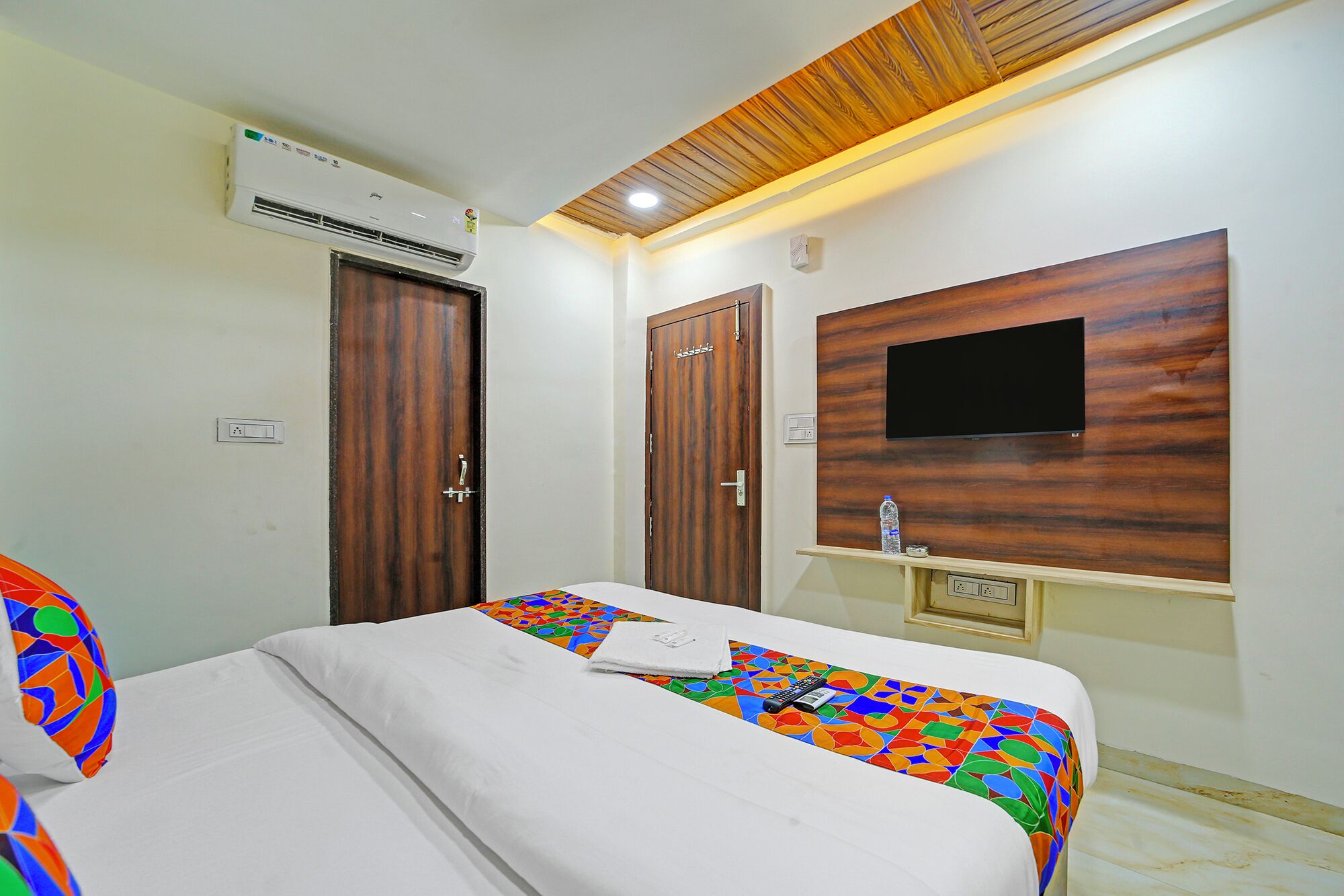 Une chambre d’hôtel avec un lit, deux portes en bois, un téléviseur fixé au mur et un appareil de climatisation.