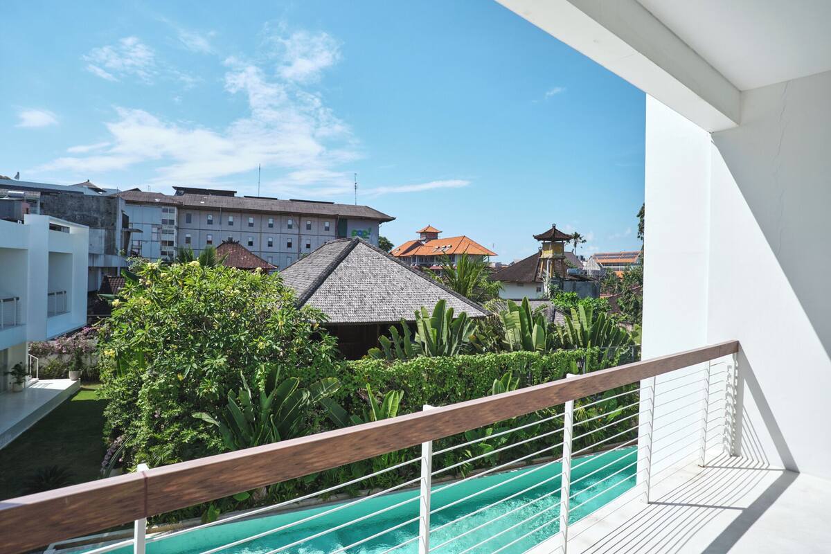A balcony with a pool, greenery, and buildings in the background.