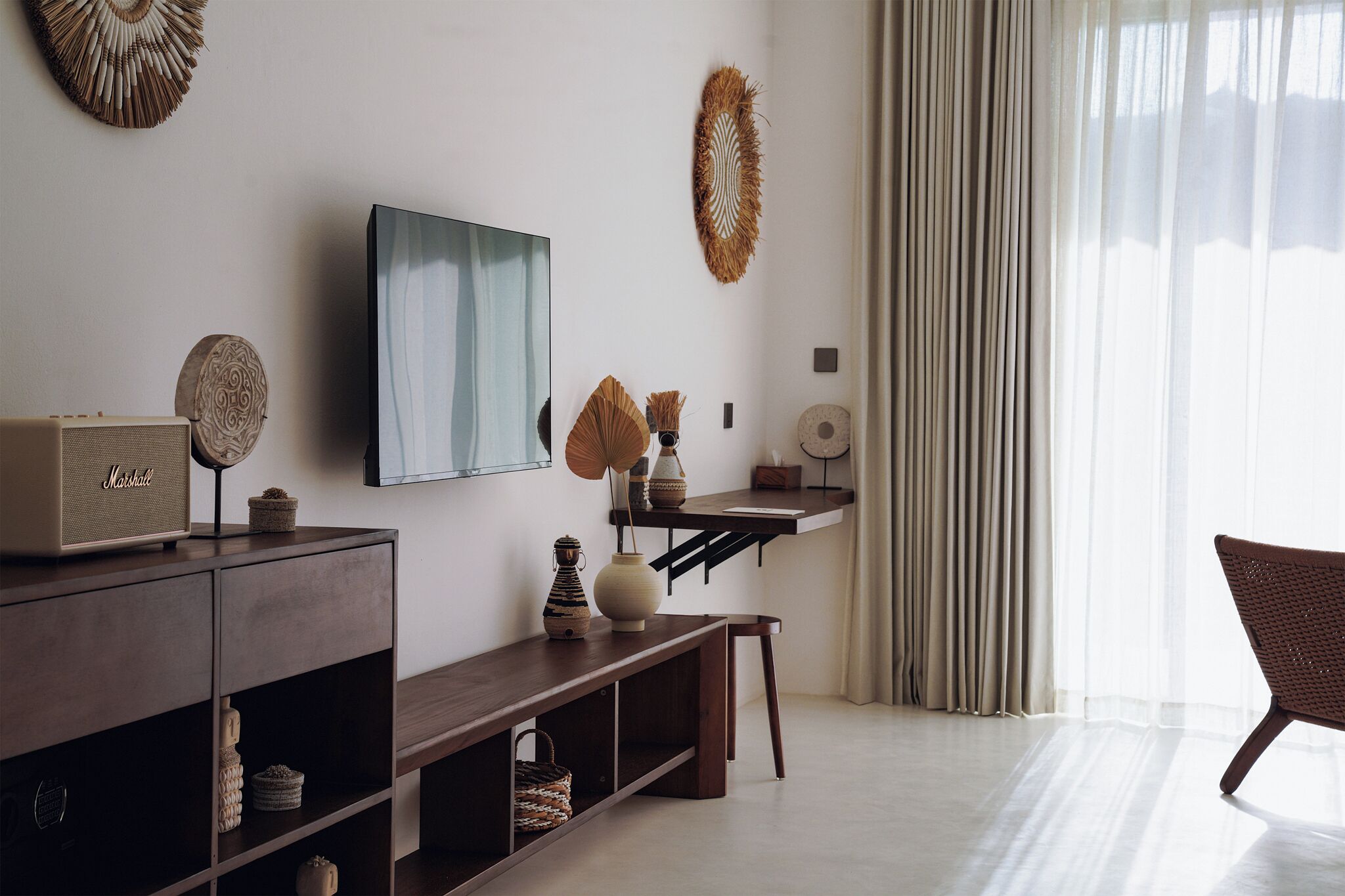 A modern living room with a wooden console table, a flat-screen TV, decorative wall art, and a wicker chair.