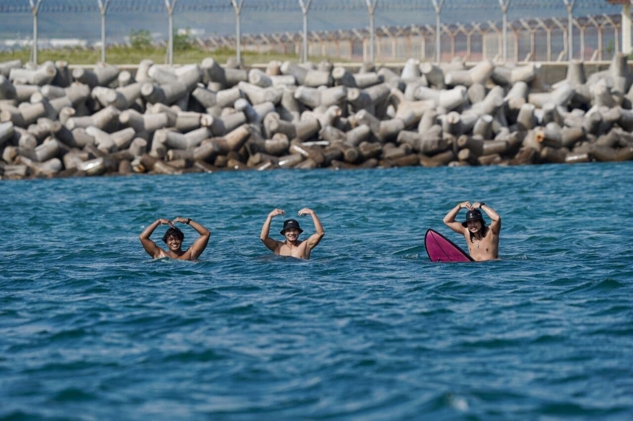 Drei Personen im Wasser vor einem steinernen Wellenbrecher.