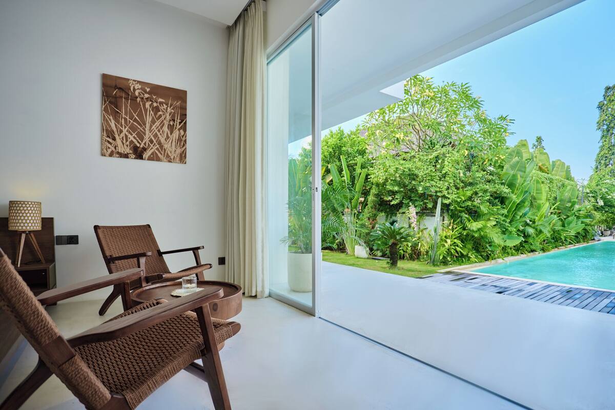 A modern room with a glass door leading to a pool, a dining area with chairs, a table, and a wall-mounted picture.