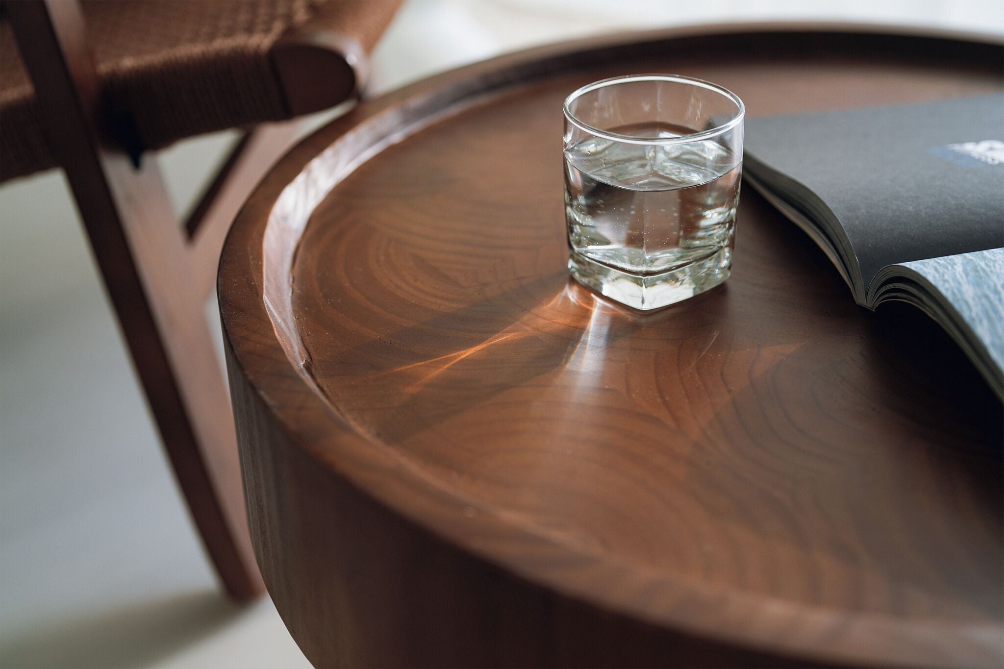 Una mesa redonda de madera con un vaso de agua y una revista abierta.