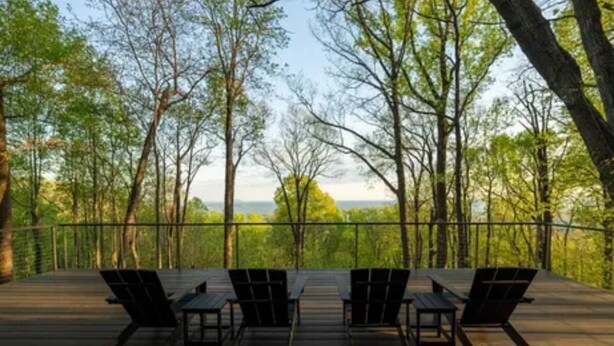 Une terrasse extérieure avec quatre chaises longues et une table, entourée d’arbres et offrant une vue sur le paysage.
