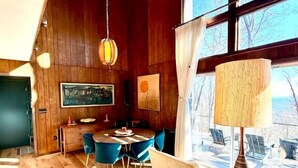 Un espace repas doté d’un plafond en bois, de grandes fenêtres et d’une table entourée de chaises.
