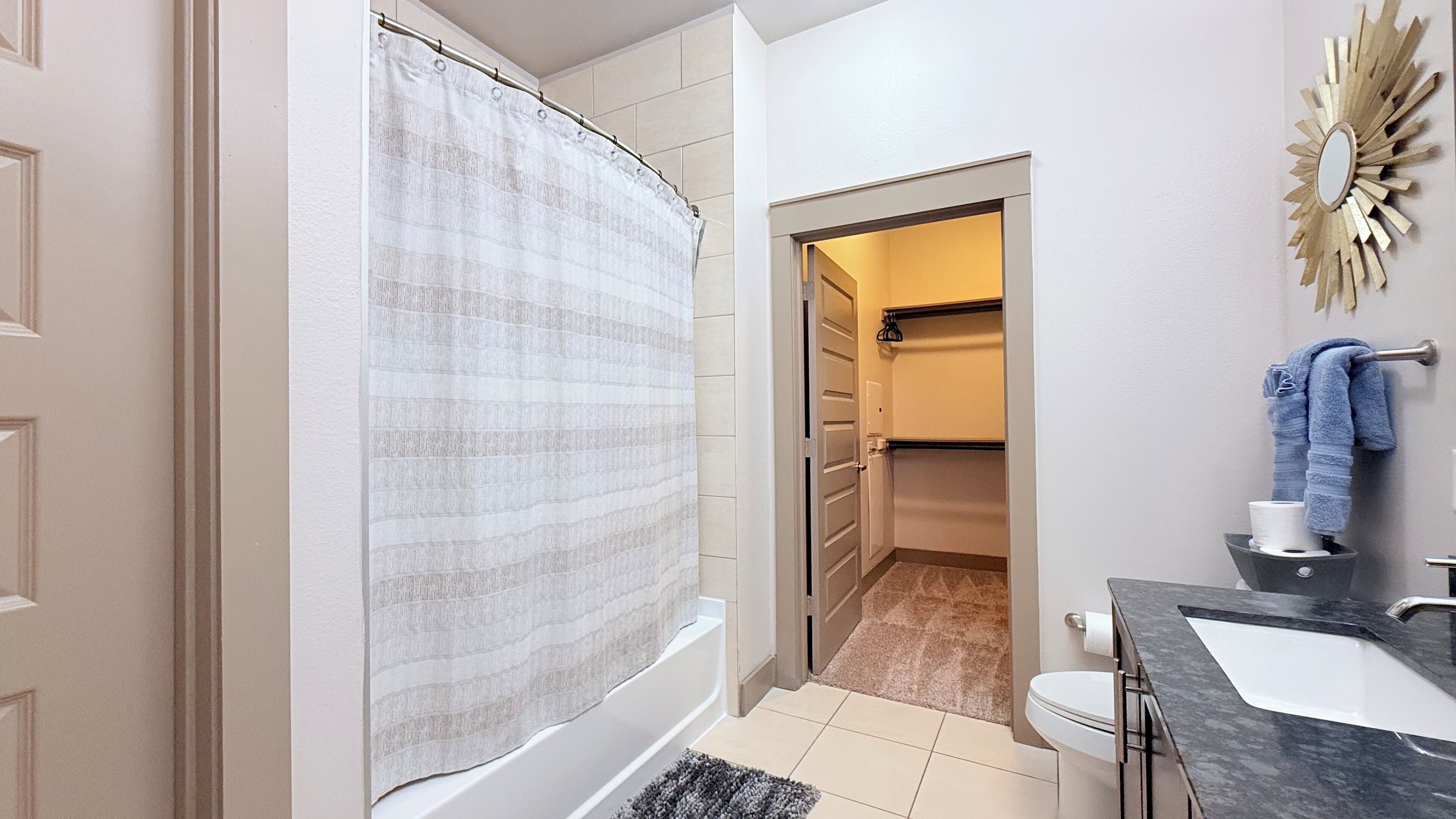 Casa de banho com cortina de chuveiro, sanita, lavatório e porta-toalhas.