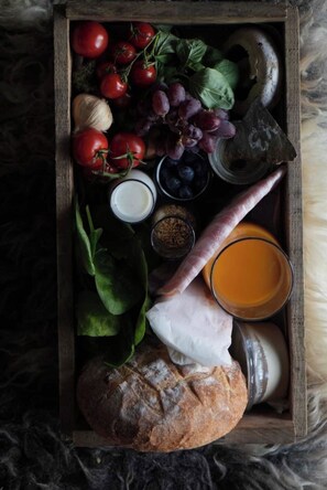 Een houten dienblad met diverse etenswaren, zoals tomaten, druiven, spinazie, kaas en brood.