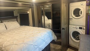 Une petite chambre comprenant un lit, un lave-linge et un miroir.