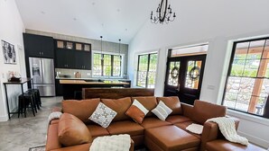 A modern living room with a sectional sofa, a patterned rug, and a kitchen in the background.