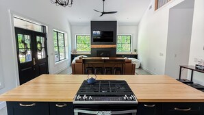 A modern kitchen with a central island, built-in oven, and a flat-screen TV above the island.