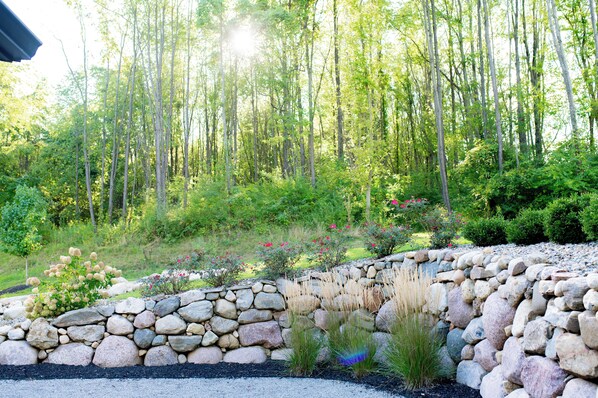 A garden with a stone wall, various plants, and a forest in the background.