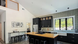 A modern kitchen with a central island, black cabinetry, and a large window providing natural light.