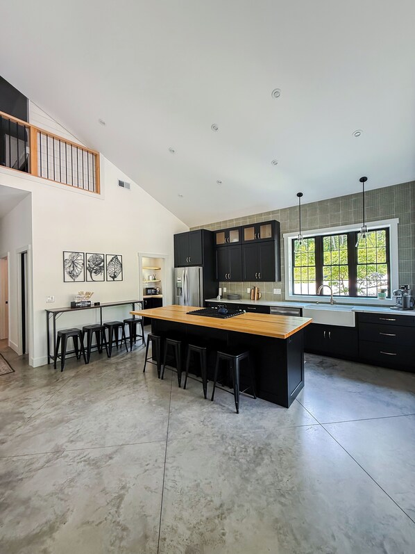 A modern kitchen with a central island, black cabinetry, and a large window providing natural light.