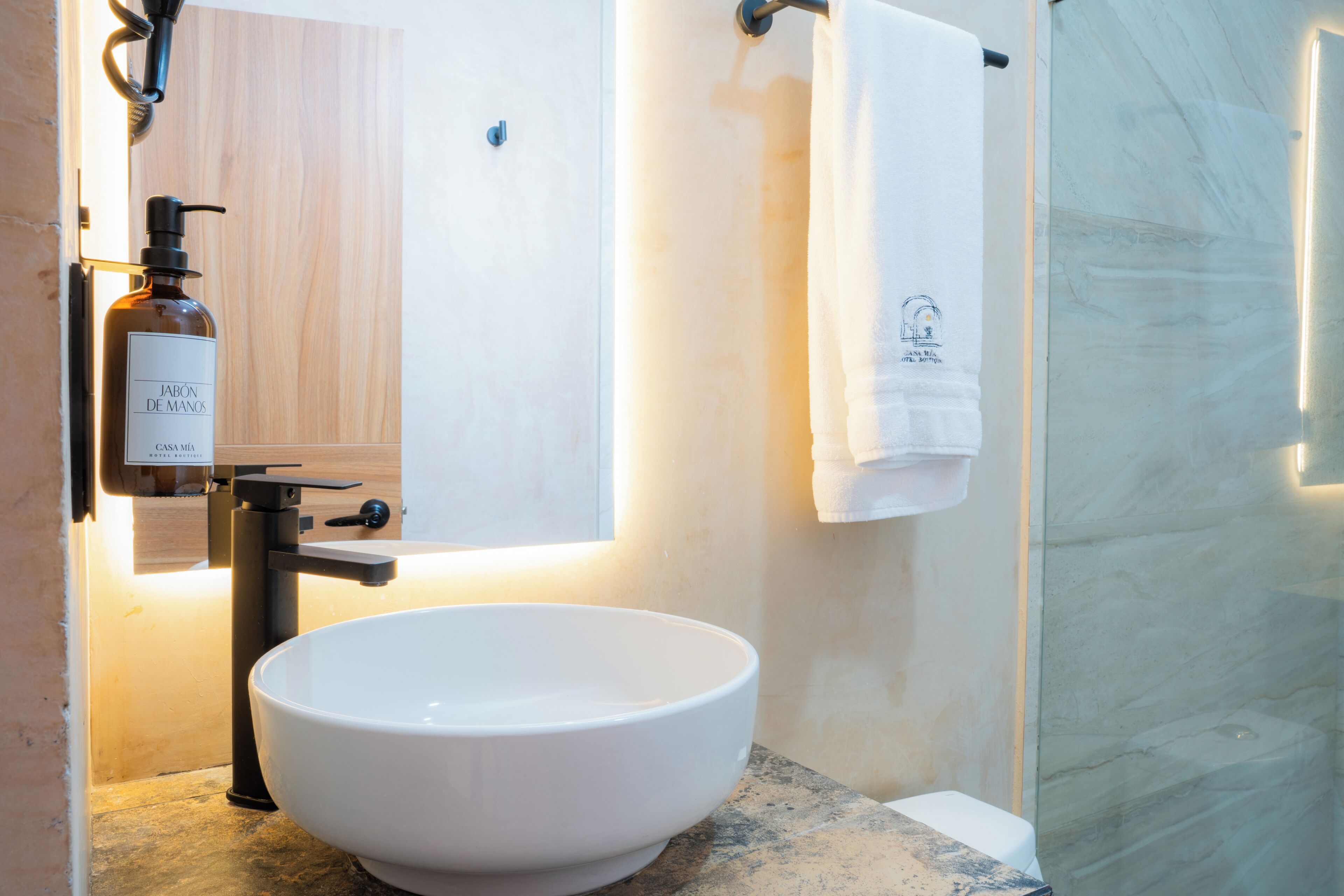 A bathroom with a white sink, a mirror, a towel, and a bottle of soap.