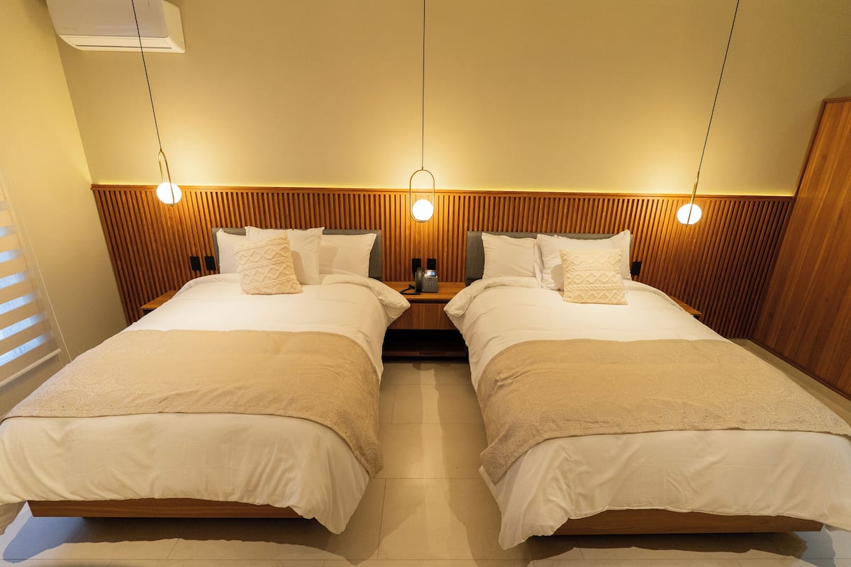 Ein Zimmer mit zwei Betten, einem Holzkopfteil, Nachttischen und Pendelleuchten.