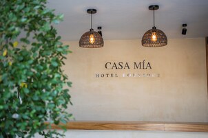 Zona de recepción con un cartel que dice 'CASA MÍA HOTEL BOUTIQUE' y dos lámparas colgantes.