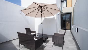 Un patio al aire libre con mesa y sillas, un gran paraguas y la entrada de un edificio.