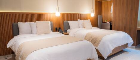 Quarto de hotel com duas camas, cabeceiras de madeira, uma mesa de cabeceira com abajur e um guarda-roupa.