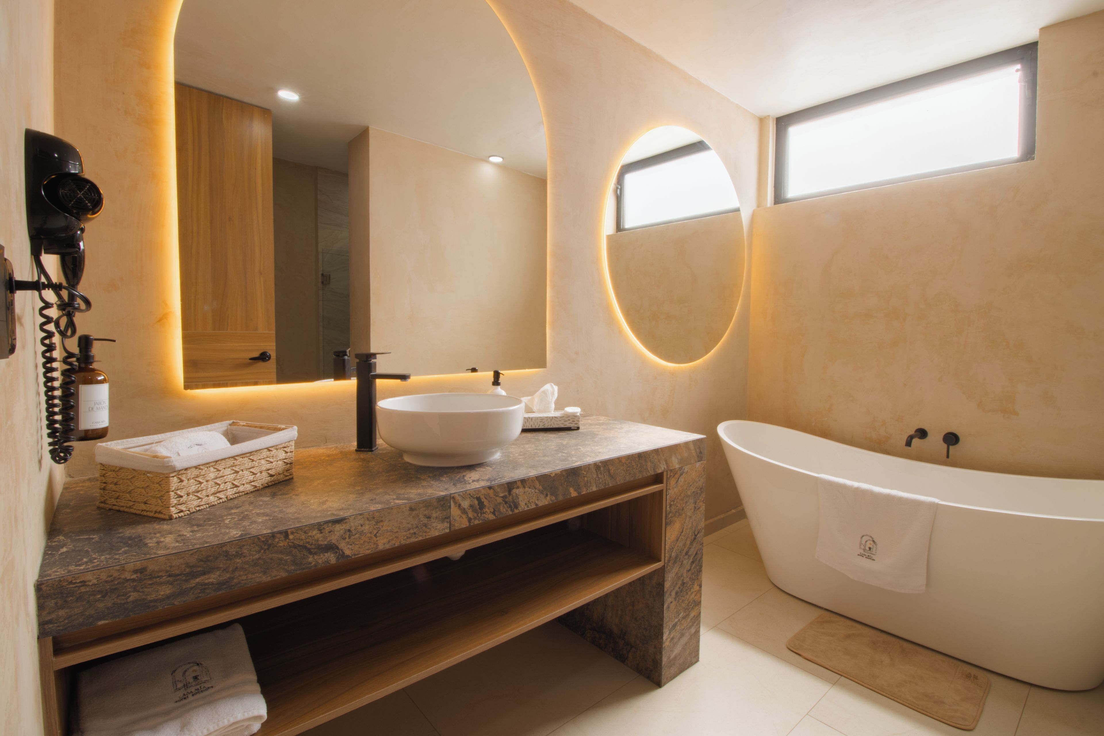 Un baño moderno con una bañera independiente, un espejo grande y un tocador con lavabo y toallero.
