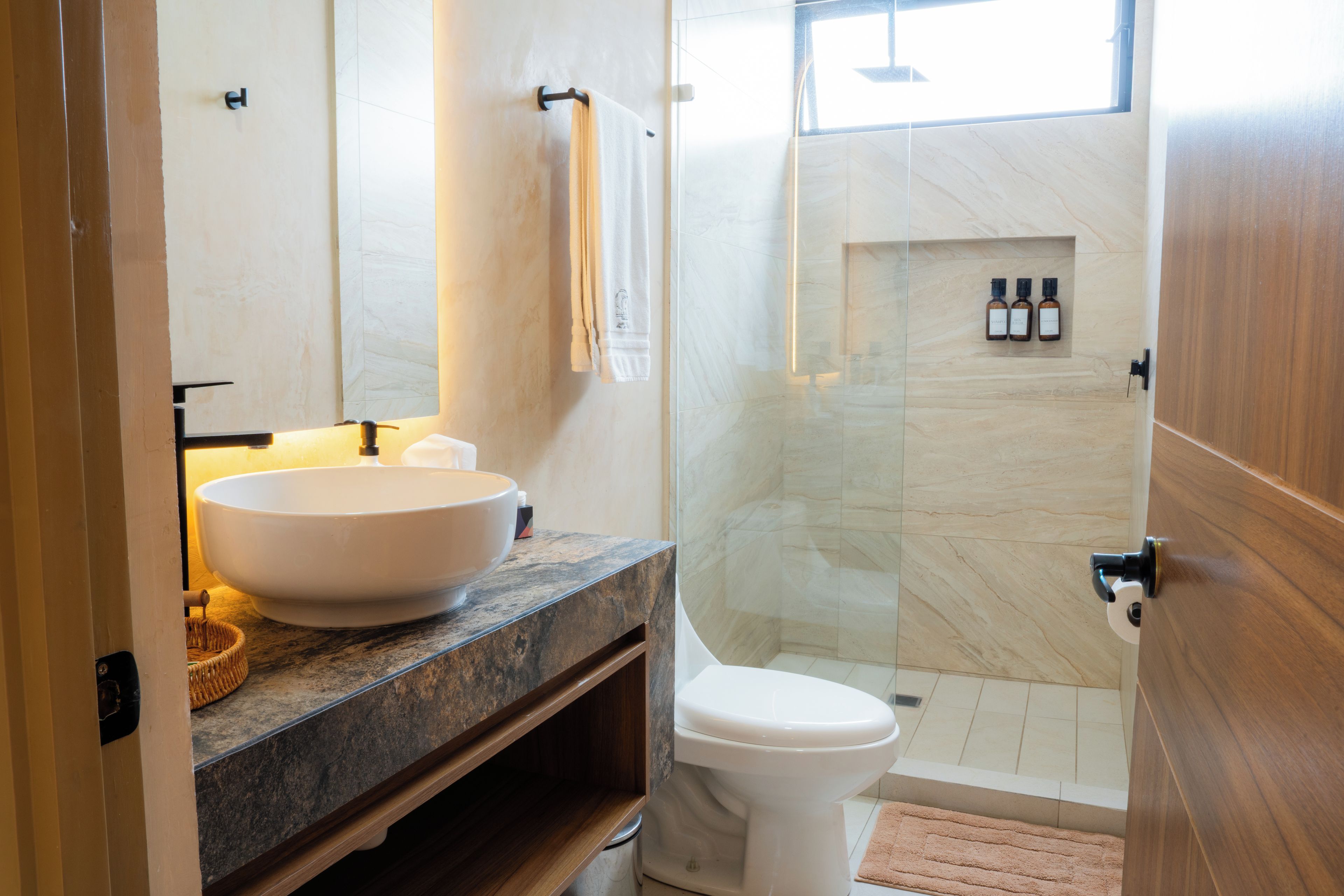 Un baño moderno con un lavamanos grande tipo recipiente, un inodoro y una zona de ducha con mampara de vidrio.