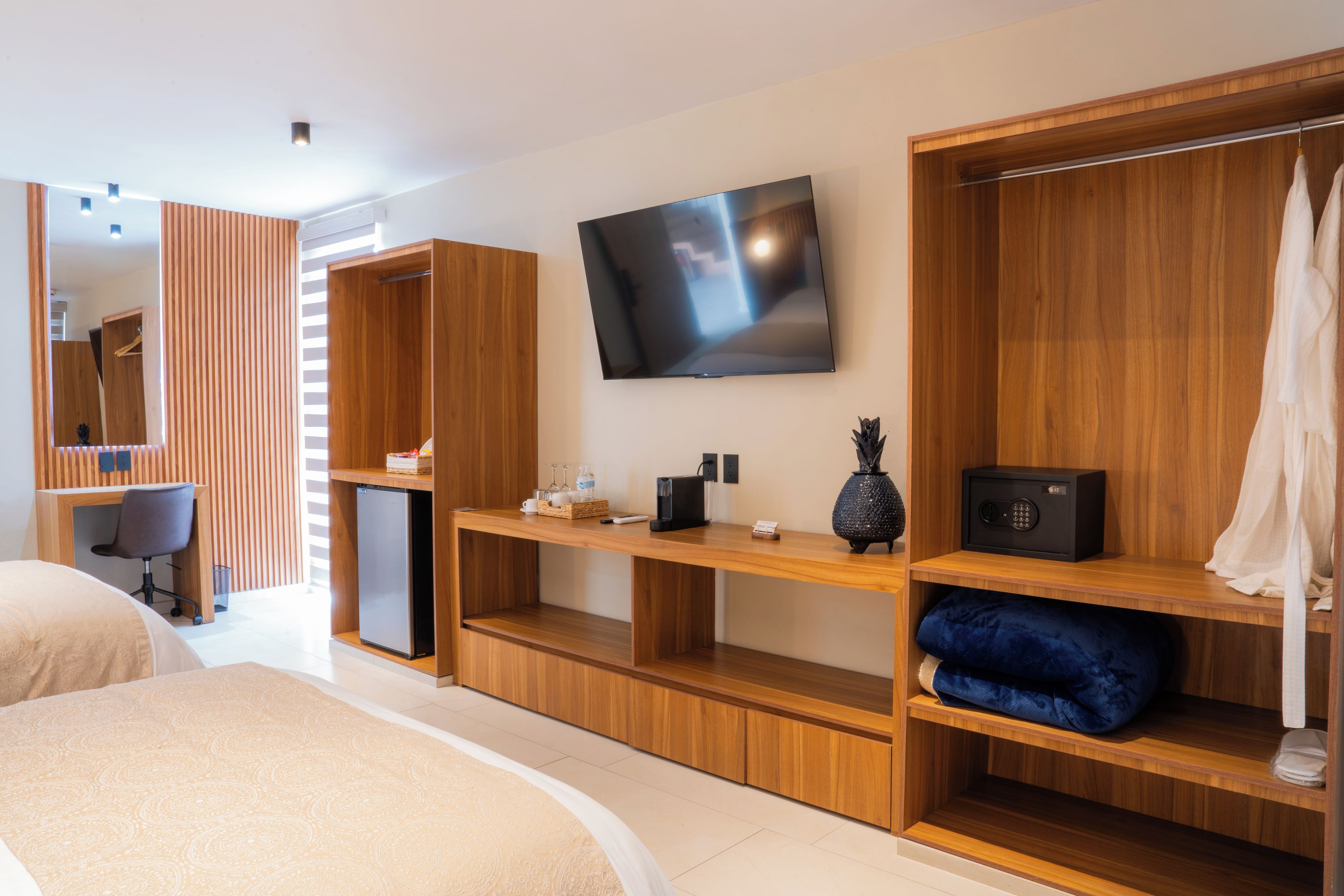 A modern hotel room with a bed, a desk, a television, and built-in wardrobes.