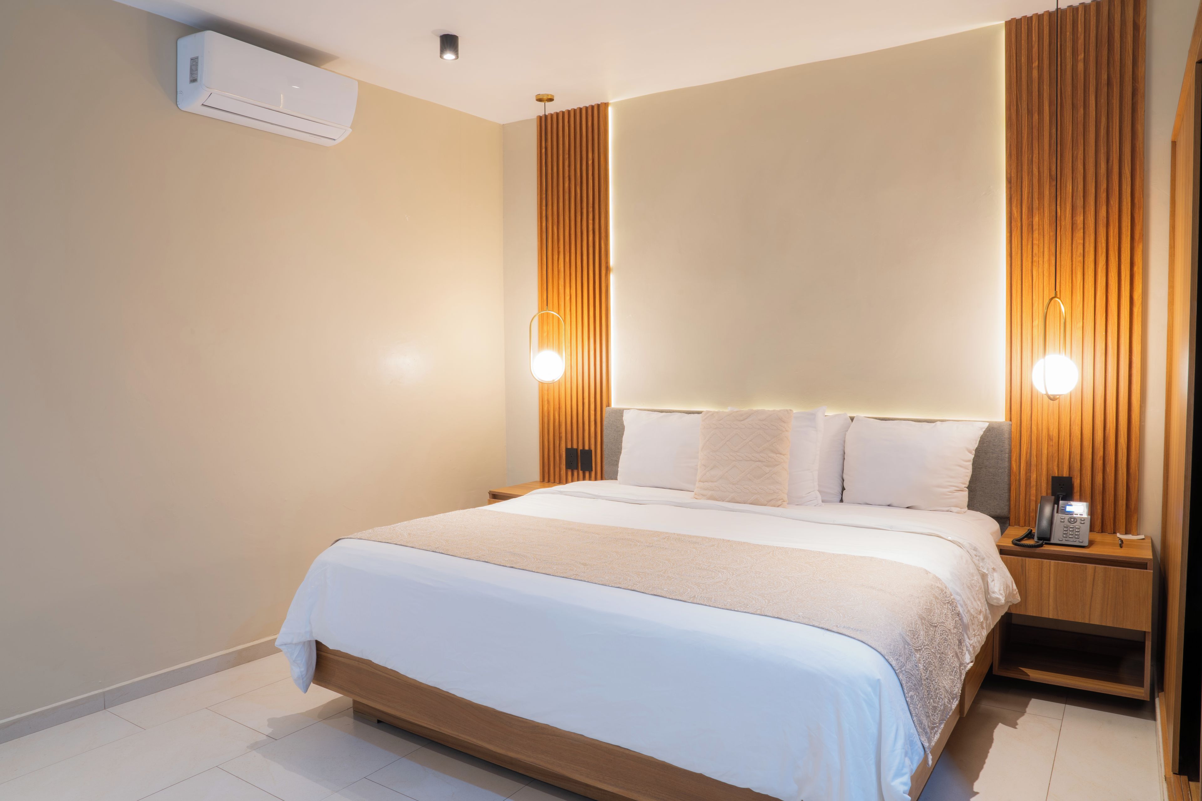 Ein modernes Hotelzimmer mit einem großen Bett, Nachttischlampen, einem Telefon und einer Wandklimaanlage.