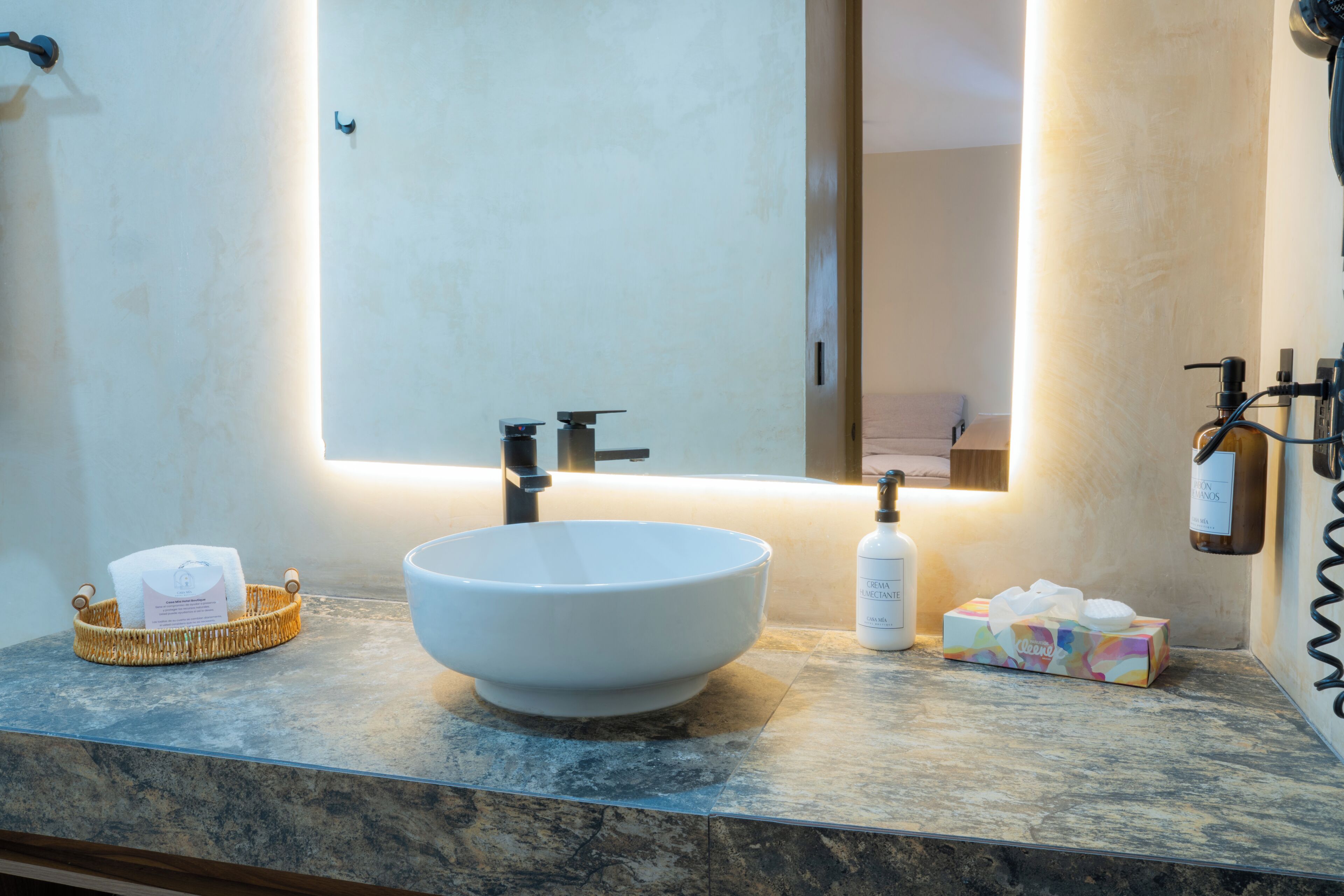A bathroom with a white sink, a mirror, and toiletries on the counter.