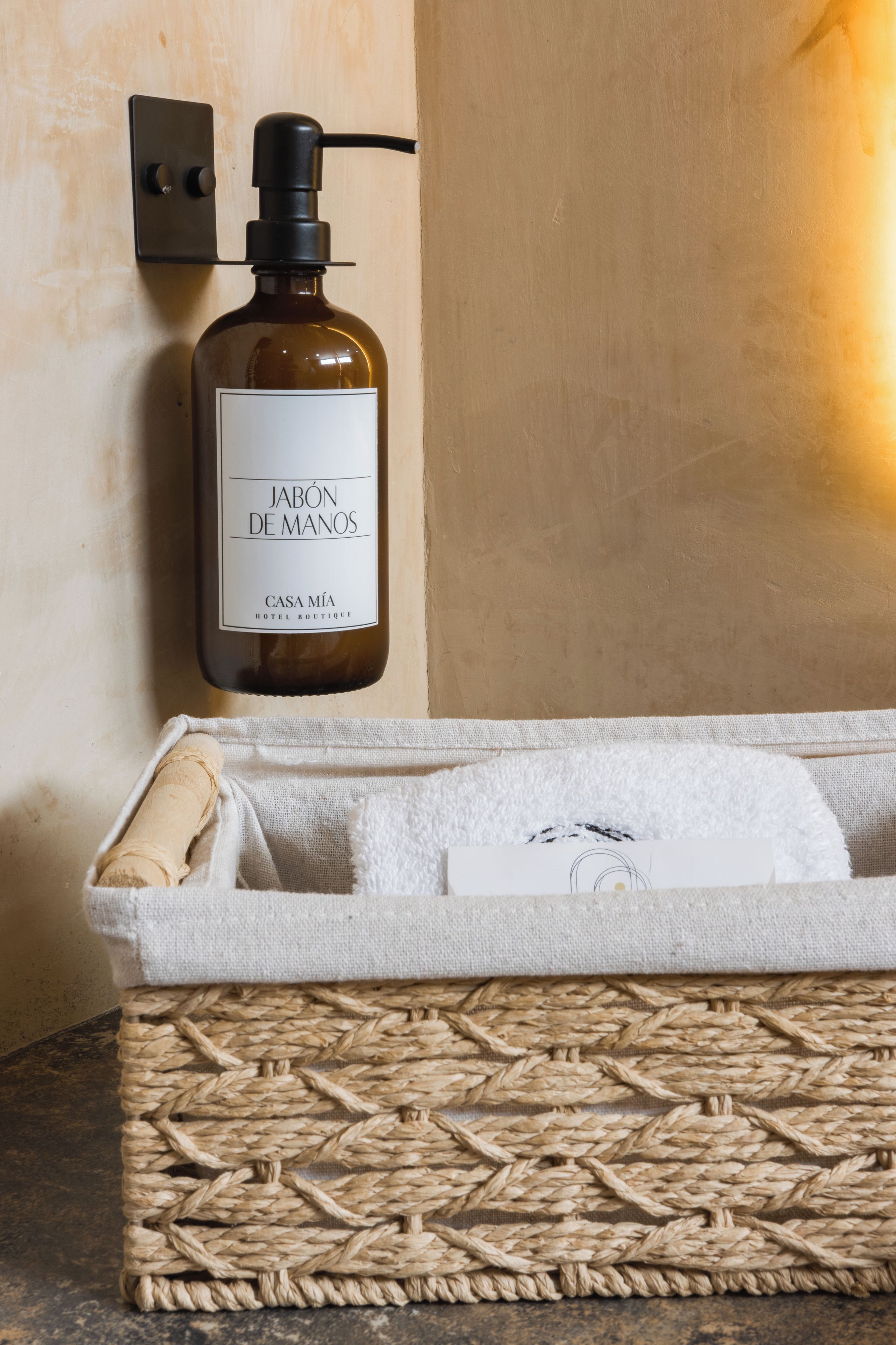 Un baño con una botella de jabón para manos, una toalla y una cesta de mimbre.