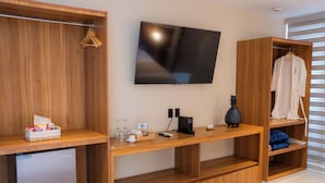 Een moderne hotelkamer met een houten tv-meubel, een flatscreen televisie, een minibar en een zithoek met een houten bankje.