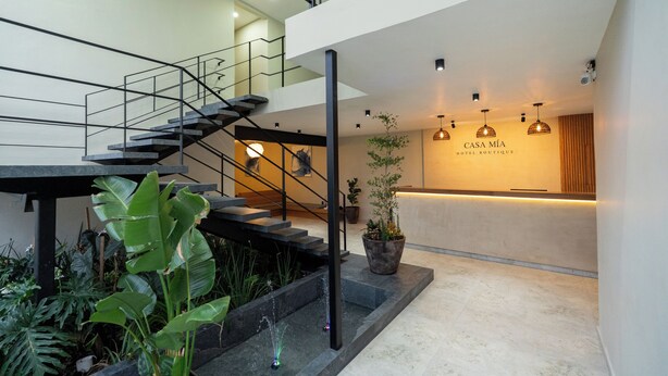 A modern hotel lobby with a reception desk, a staircase, and indoor plants. - Casa Mia Hotel Boutique (Zamora)