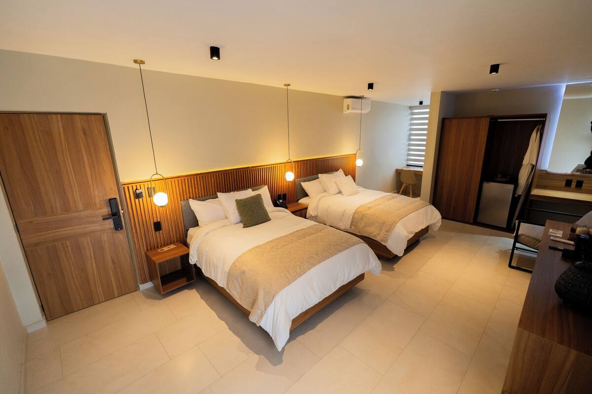Ein modernes Hotelzimmer mit zwei Betten, Holz-Kopfteilen, Nachttischen und einem eingebauten Kleiderschrank.