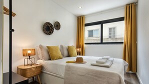 Een slaapkamer met een bed, nachtkastjes, een raam met gordijnen en decoratieve wandversieringen.