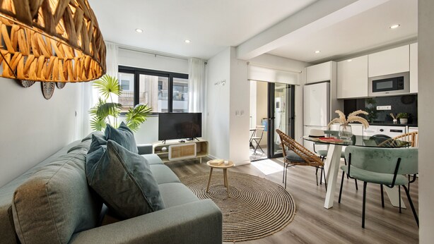 Een moderne woonkamer met een bank, televisie en een eetgedeelte met stoelen en een tafel.