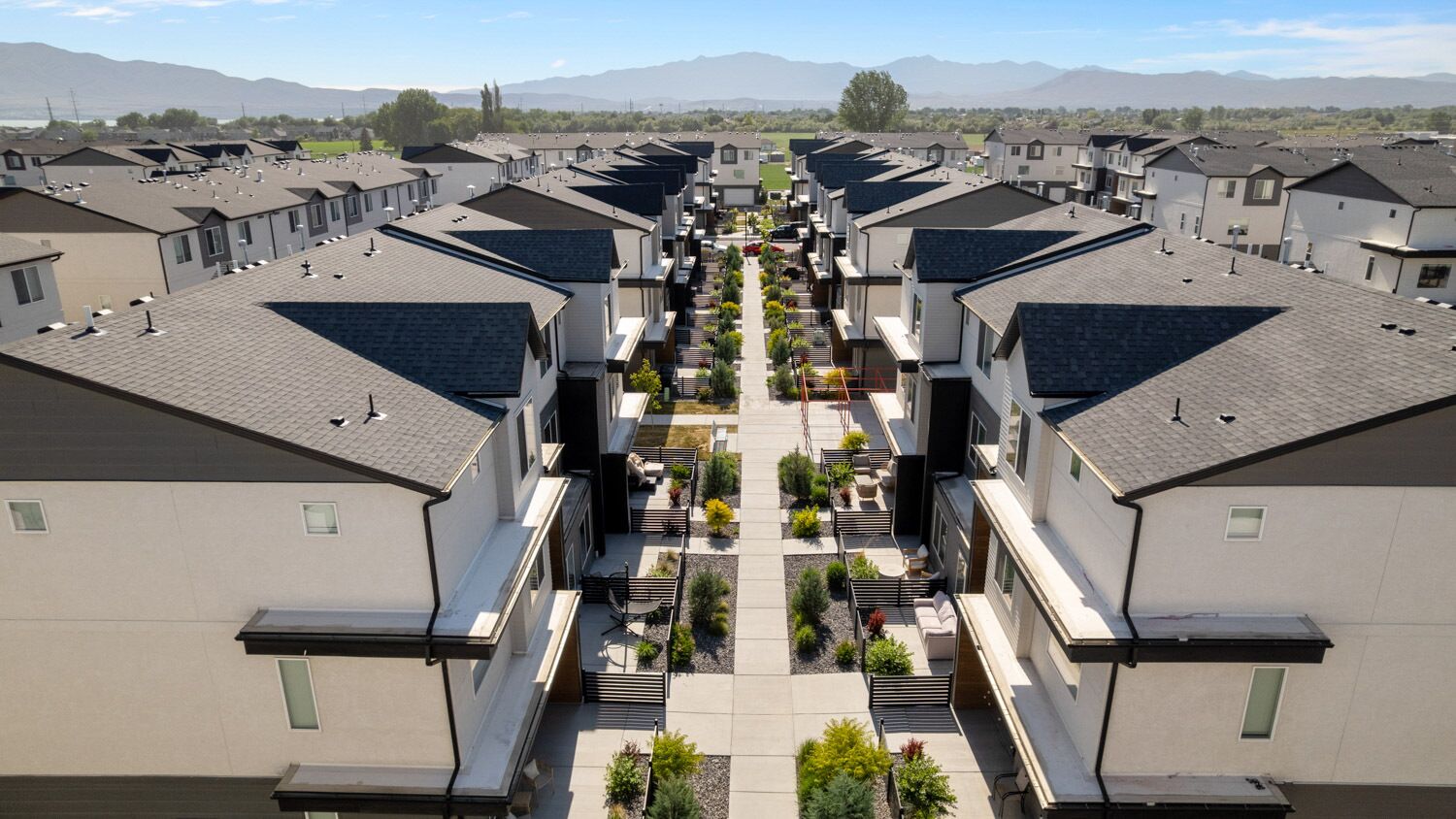 Un complejo residencial con varias casas de dos pisos, un patio central con asientos y plantas, y montañas al fondo.