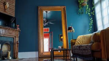A room with a large mirror, a ceiling fan, a yellow sofa, and a fireplace.