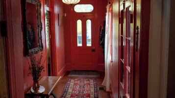 A hallway with a red door, a mirror, a vase with dried flowers, and a patterned rug.