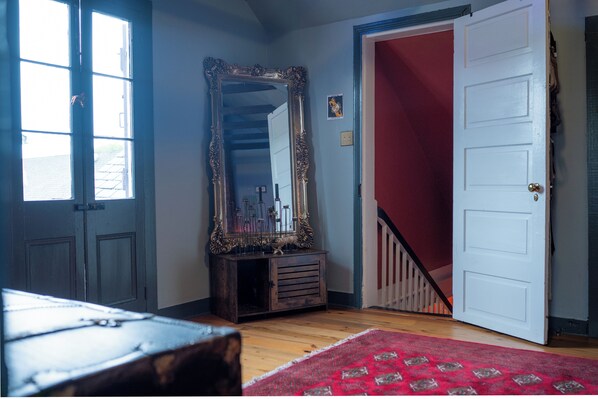 Quarto com cômoda de madeira, espelho, tapete vermelho e escada que leva a uma área com paredes vermelhas.