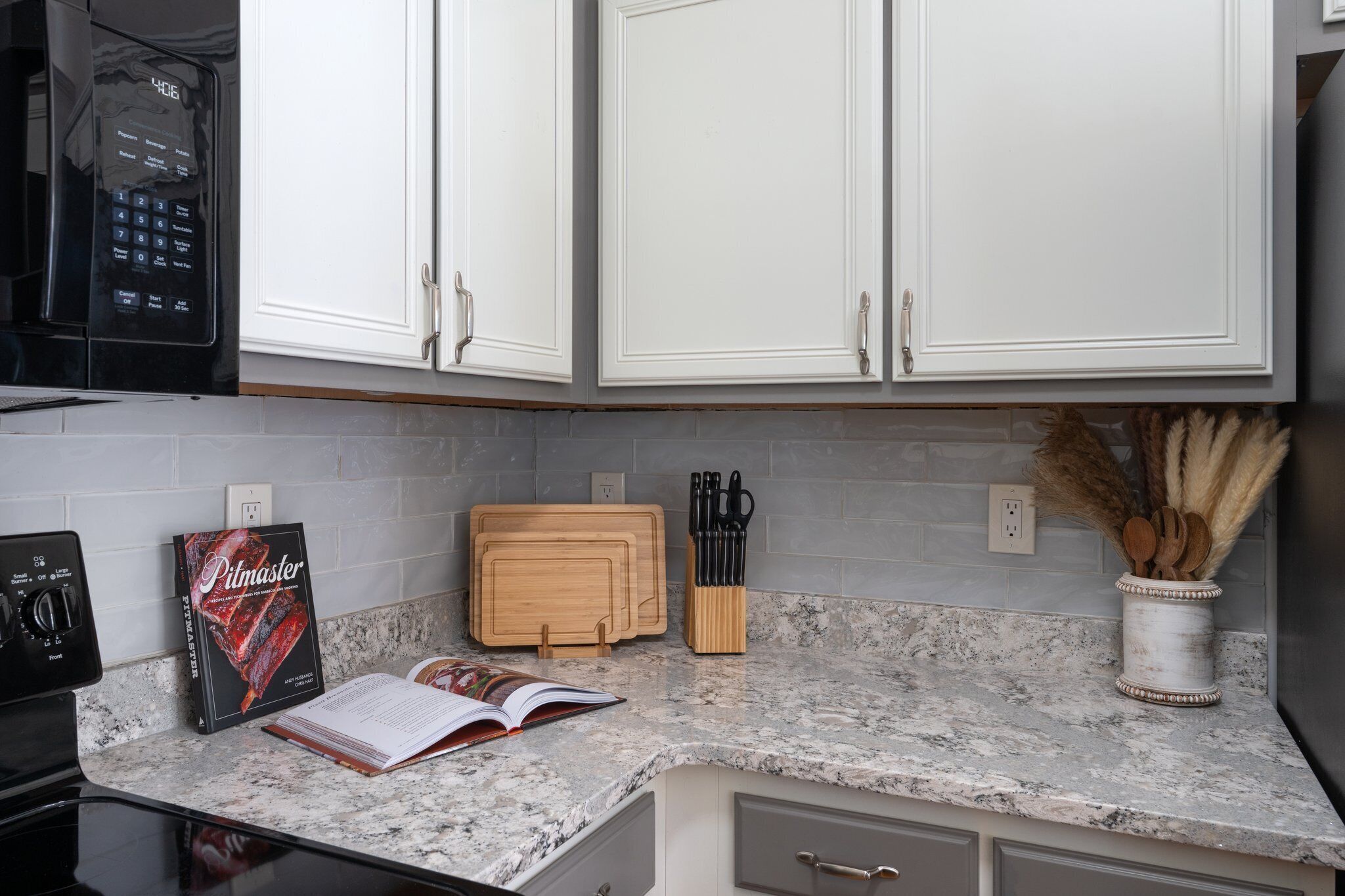 A kitchen with white cabinets, a granite countertop, a microwave, a book, a cutting board, and a knife block.