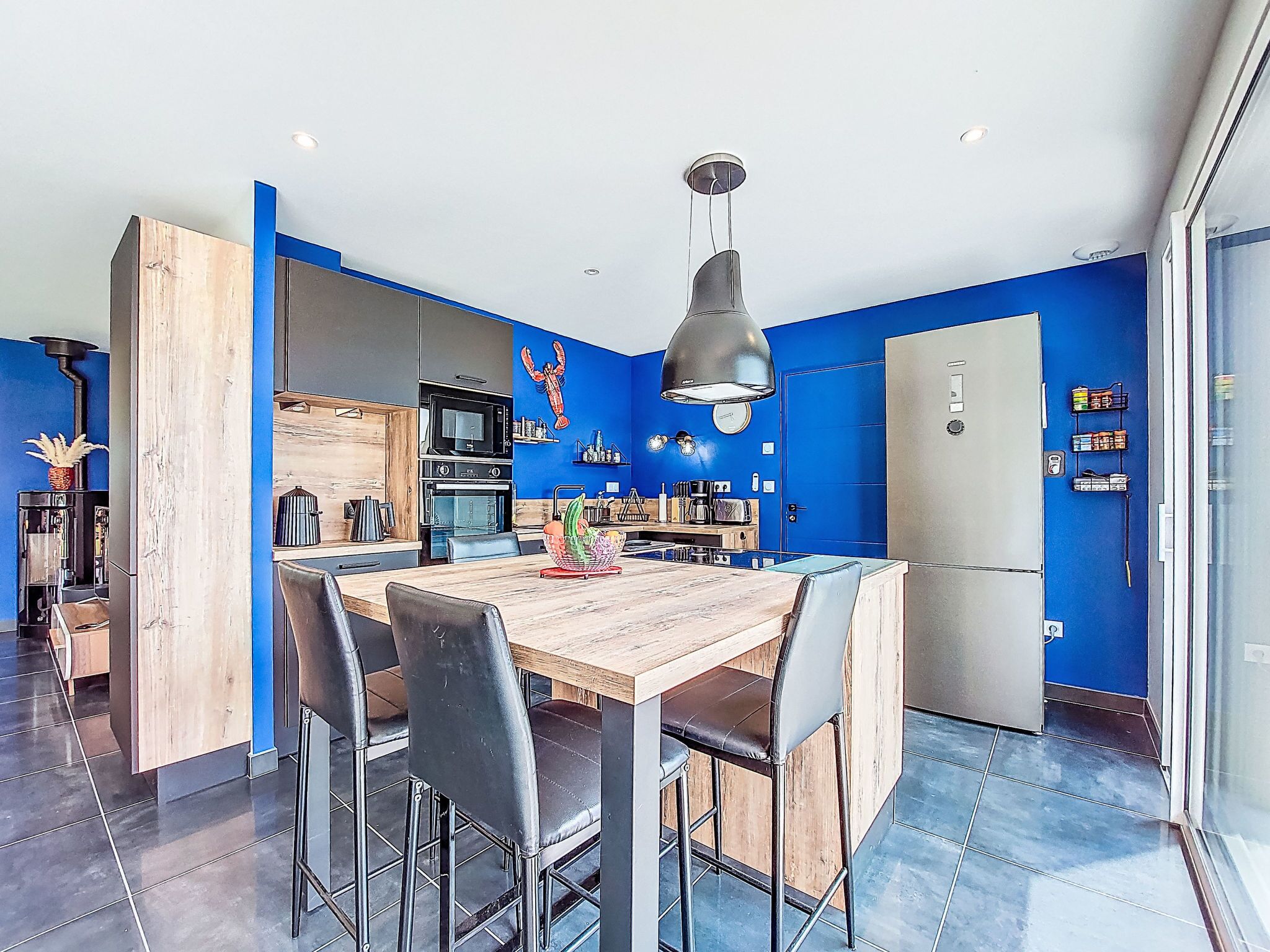 Una cocina moderna con paredes azules, una mesa de comedor de madera y sillas negras.